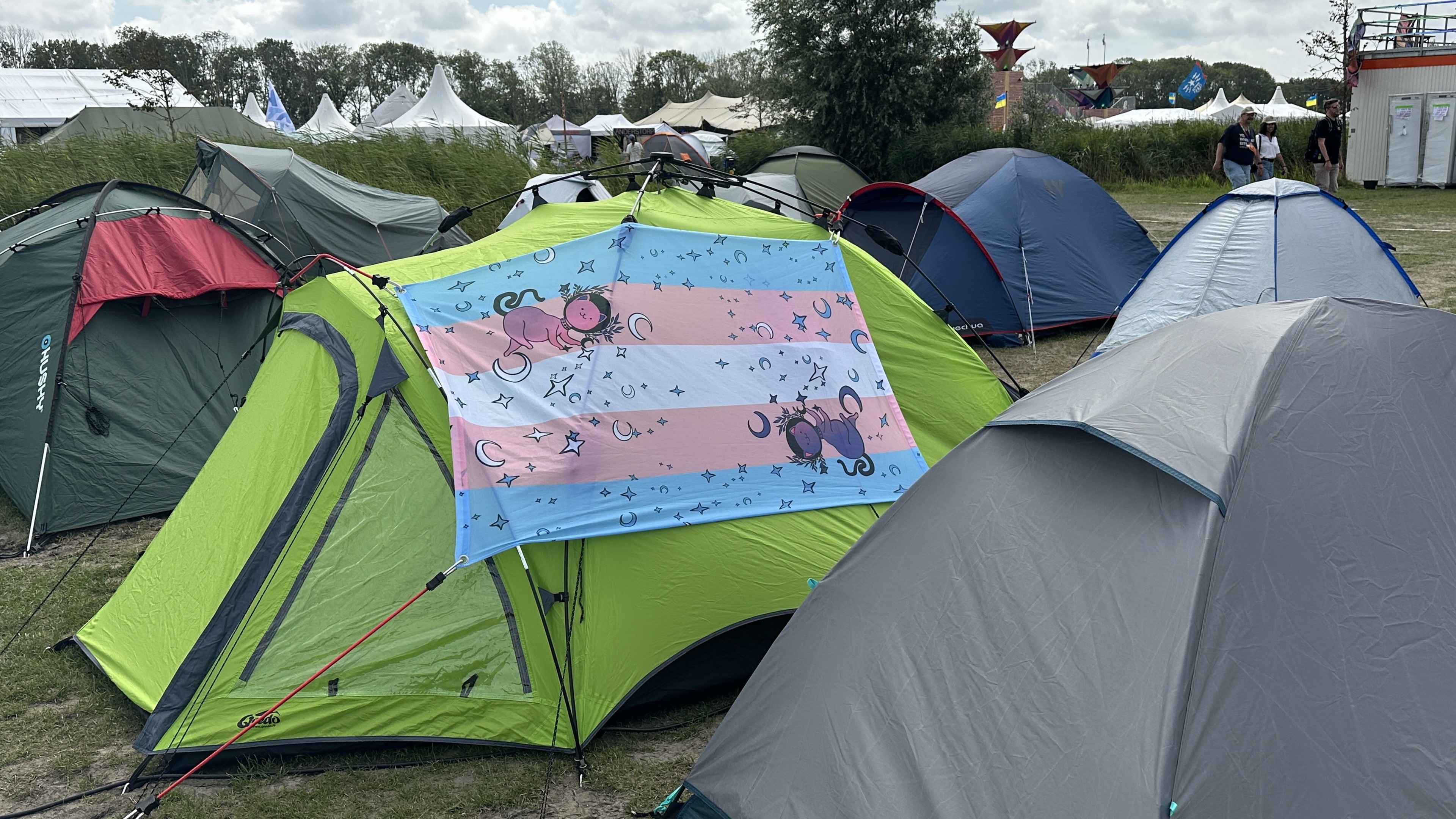 Trans pride flag on a tent. The flag also has cartoon cats and stars and moons on it
